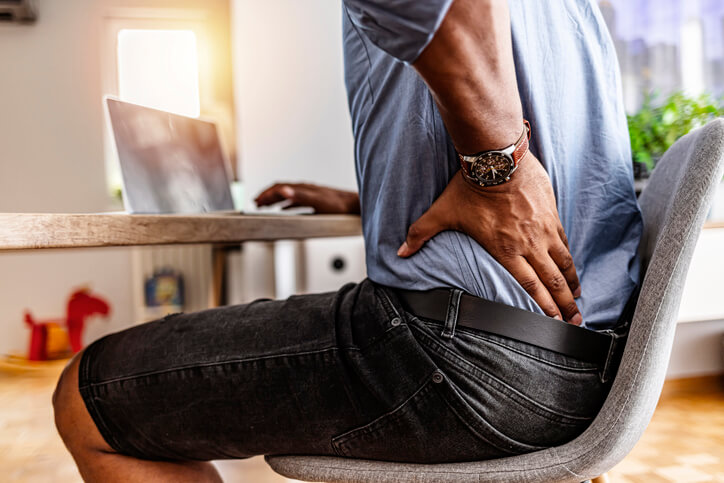 Shot of a young businessman suffering from a backache while working at his desk in his office.